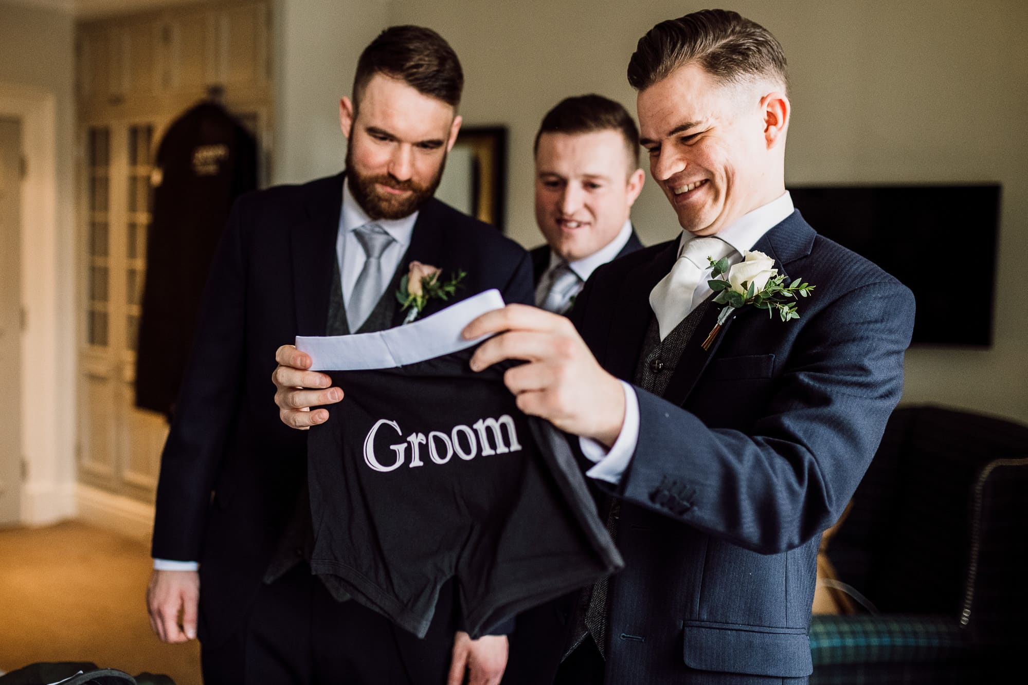 Crabwall Manor Wedding Photography | Mark & Beth 8 The groom opens up his gifts from his bride and is holding up some groom boxer shorts
