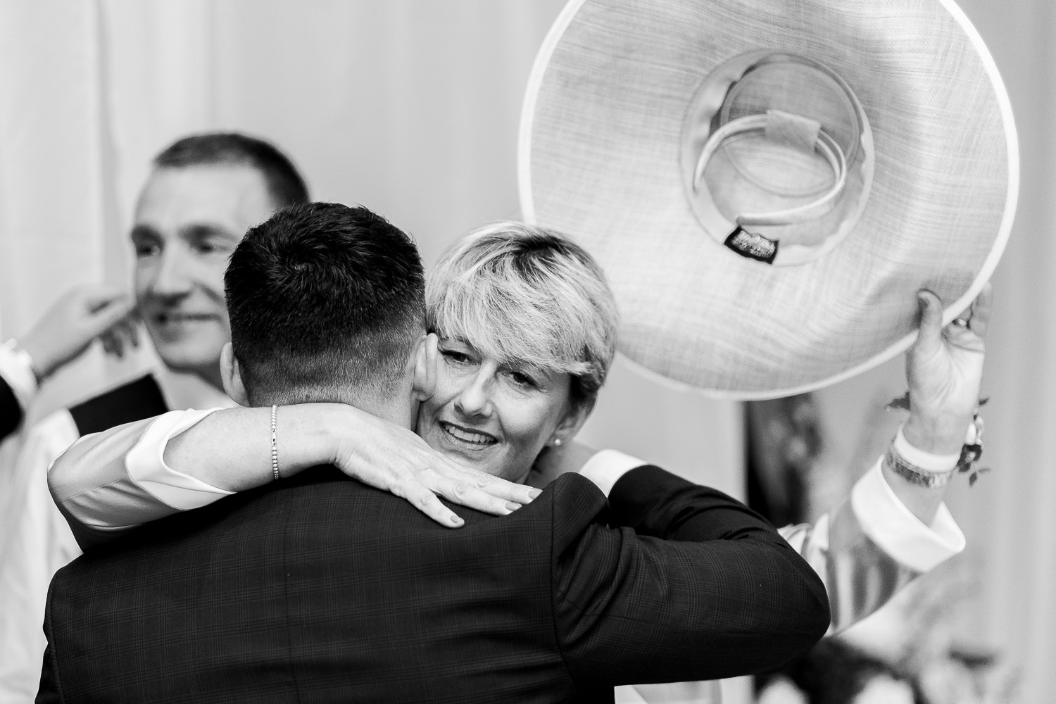 Bride's mum hugging groom and holding her hat