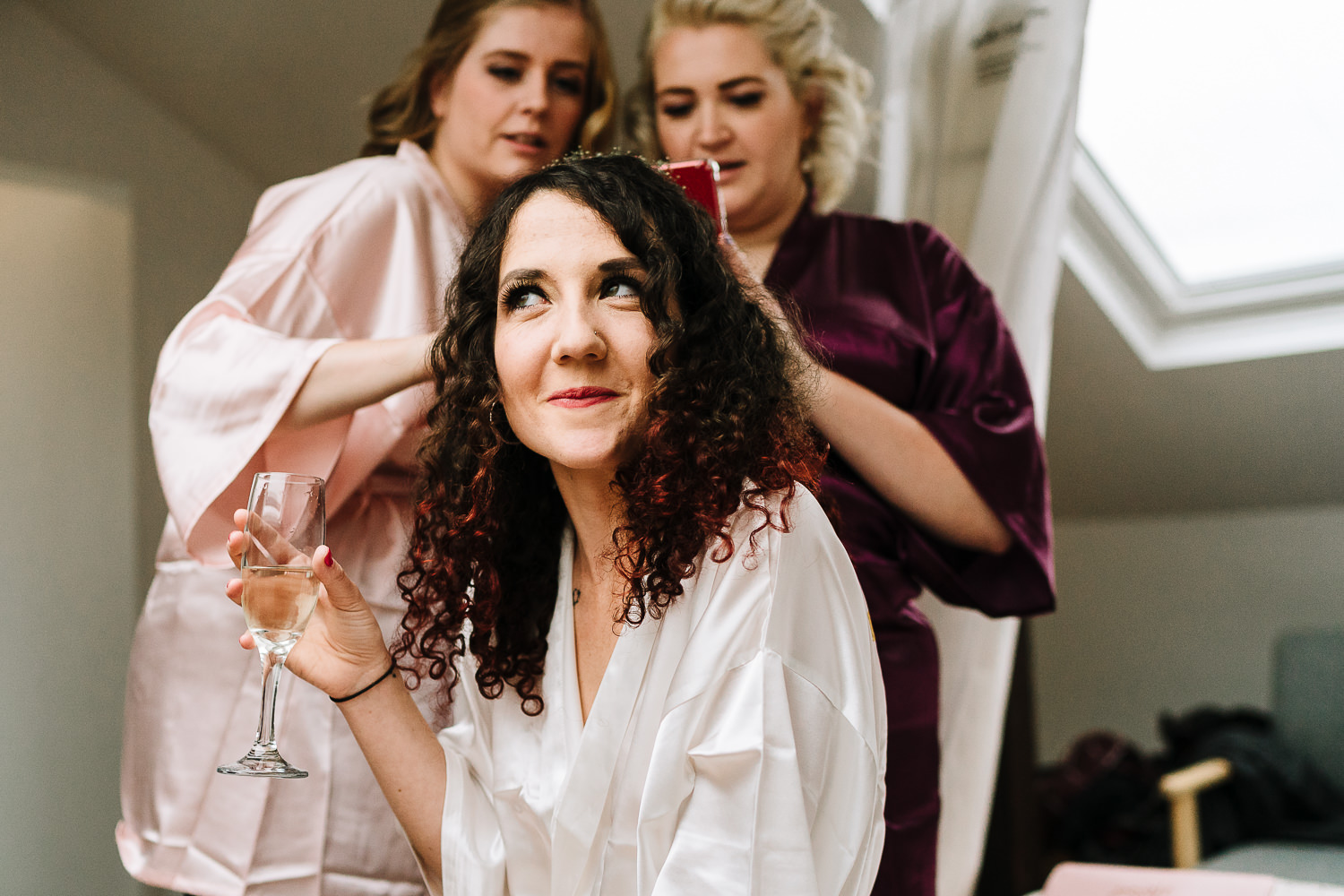 bride doing her hair and bridesmaids taking photos before going to Ashton Memorial